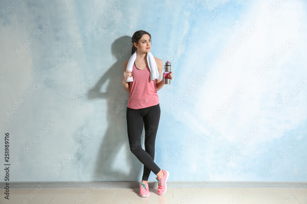 Sporty young woman with bottle of water near color wall