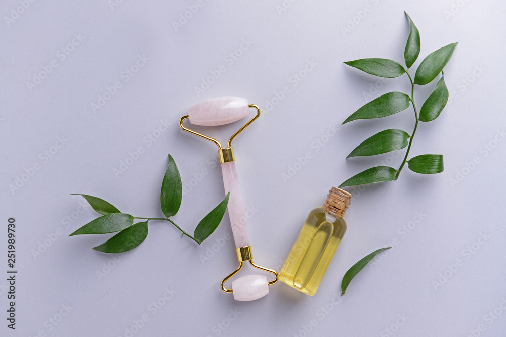 Facial massage tool with essential oil on light background