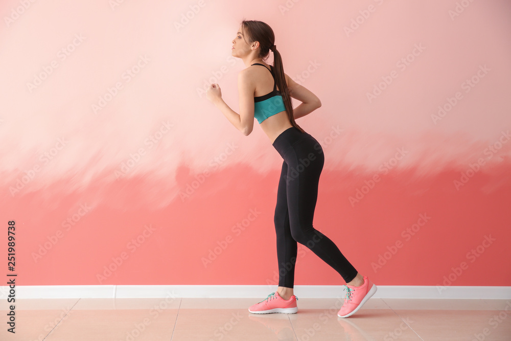 Sporty young woman running against color wall