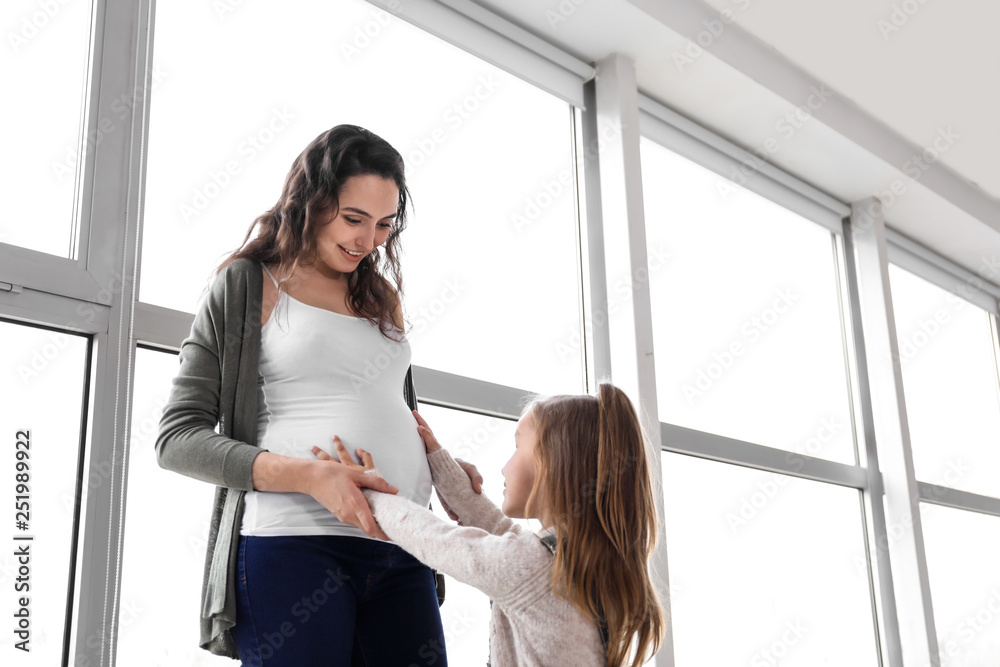 Little girl with pregnant mother near window at home