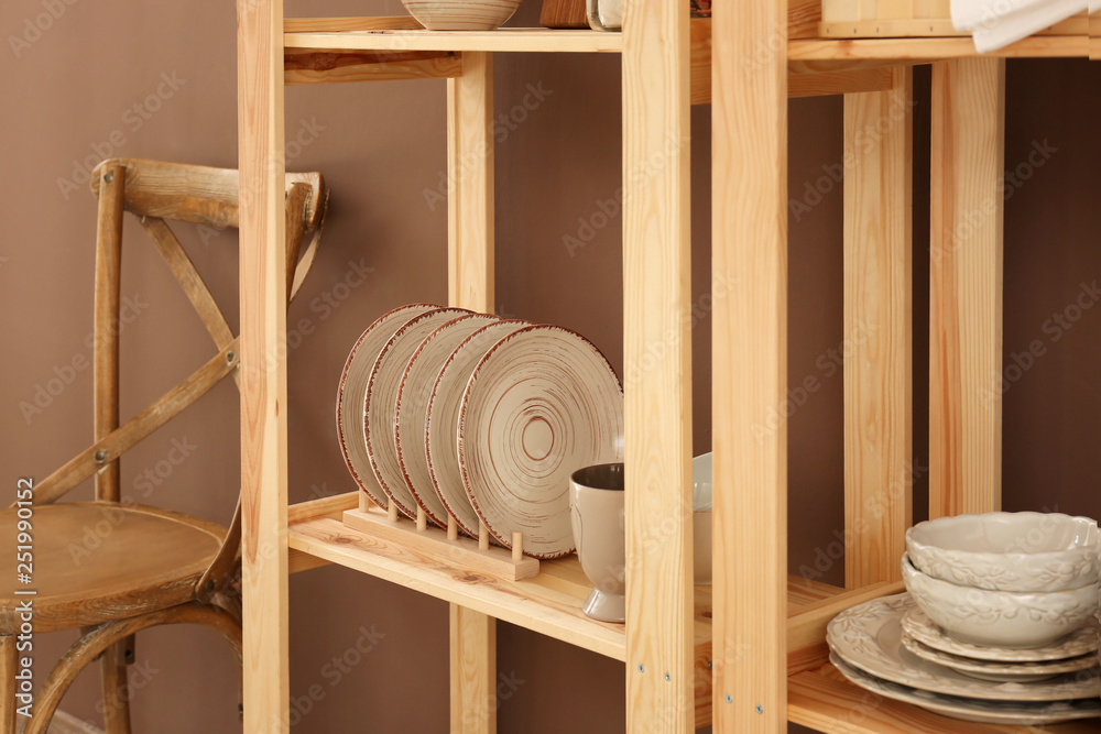 Set of clean dishes on wooden shelves near color wall