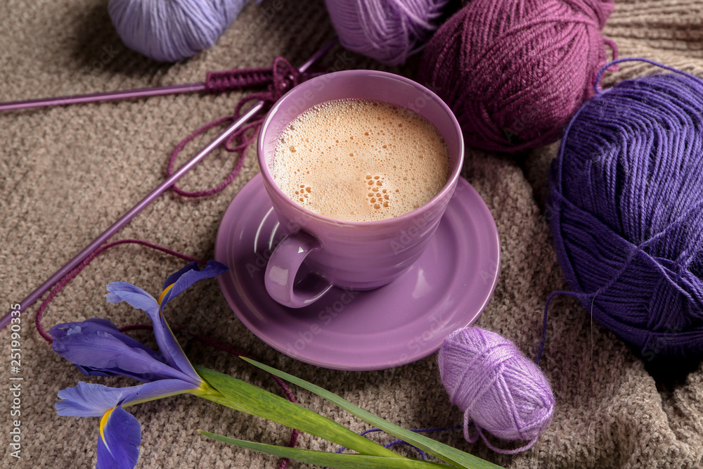 Cup of coffee with knitting yarn and flower on plaid