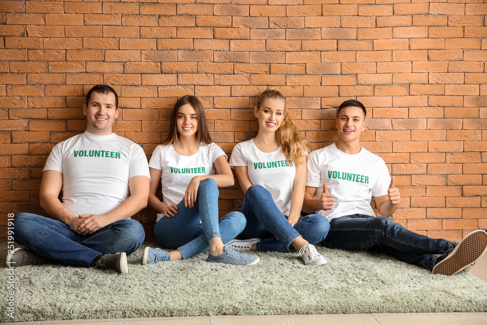 Team of young volunteers sitting near brick wall