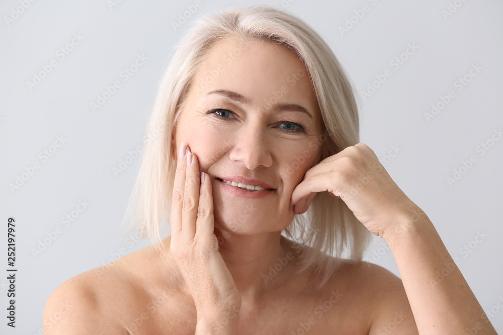 Mature woman giving herself face massage on light background