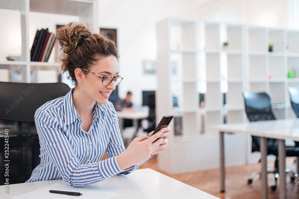 Positive young woman using mobile phone at work.