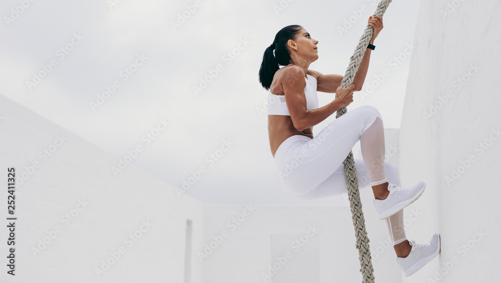 Athletic woman climbing a wall using a battle rope