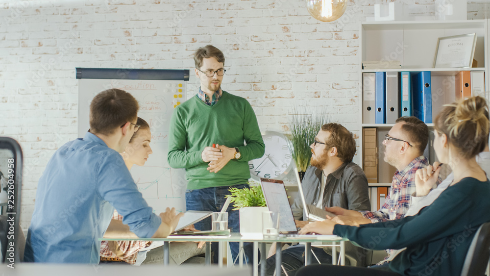 Energetic Man Does Whiteboard Presentation to His Creative Office Staff. Coworkers Sit at the Big Gl