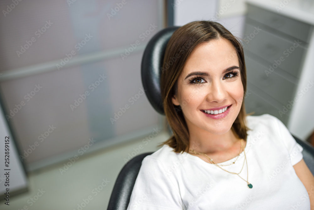 Portrait of a beautiful smiling female patient at dentist chair.