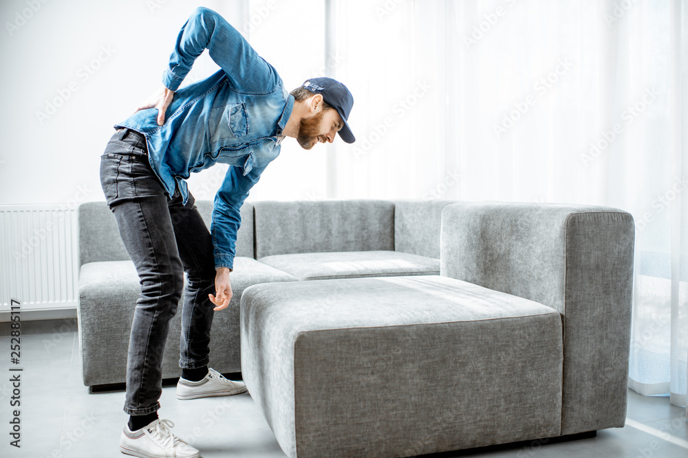 Delivery man suffering from the back ache while moving the couch in the apartment