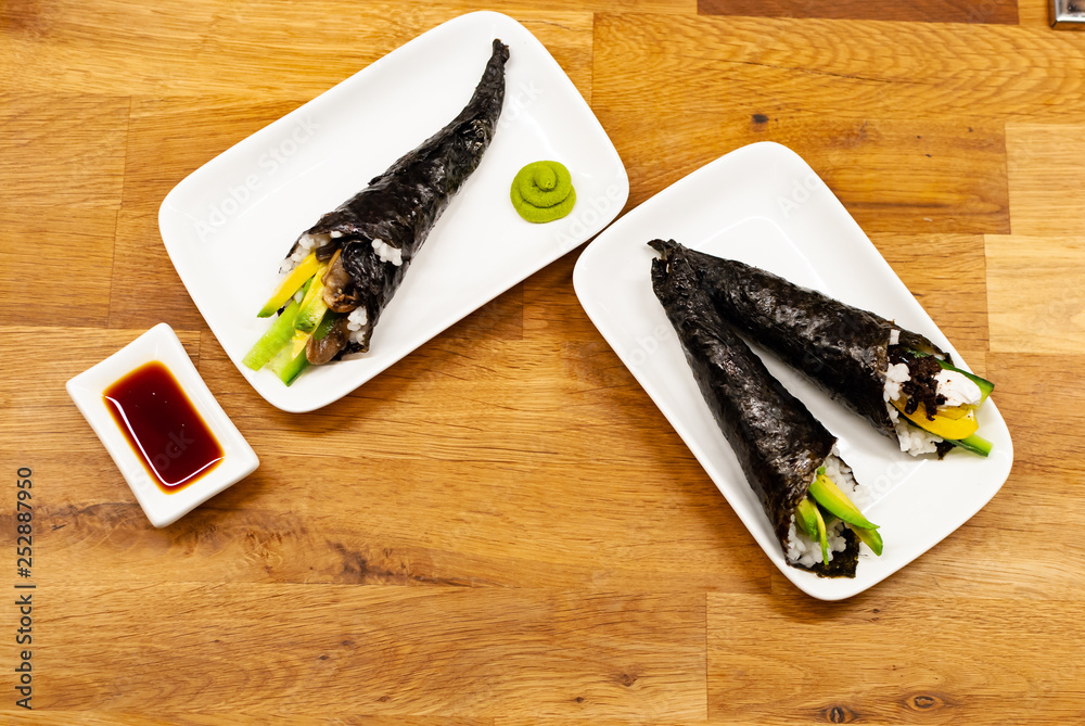 Homemade vegan Temaki-Sushi filled with avocado on a small plate on a wooden table with soy sauce an