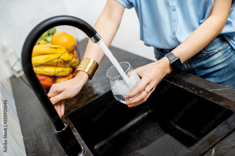 Woman filling glass with tap water for drinking on the kitchen