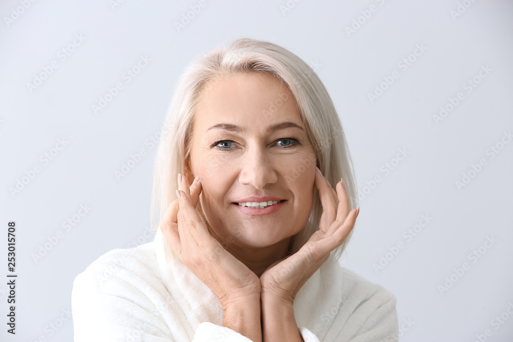 Mature woman giving herself face massage on light background