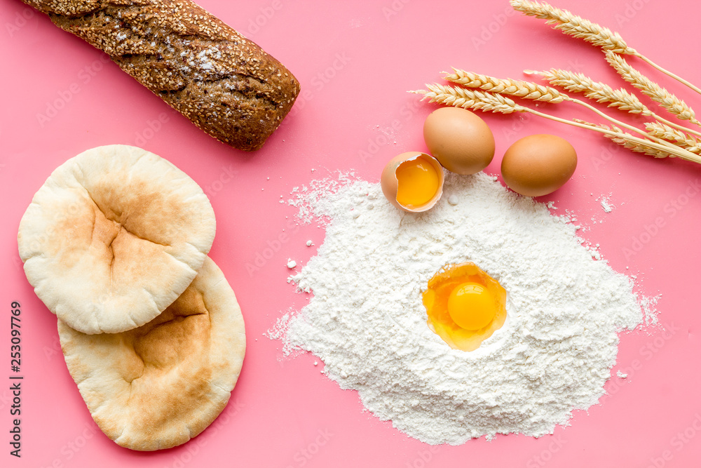 Ingredients for homemade bread. Bread near wheat ears, flour and eggs on pink background top view