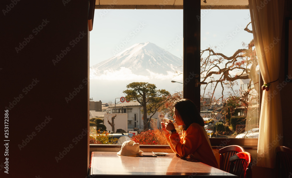 年轻的亚洲女人在酒店的窗户边欣赏富士山的景色，早上喝咖啡