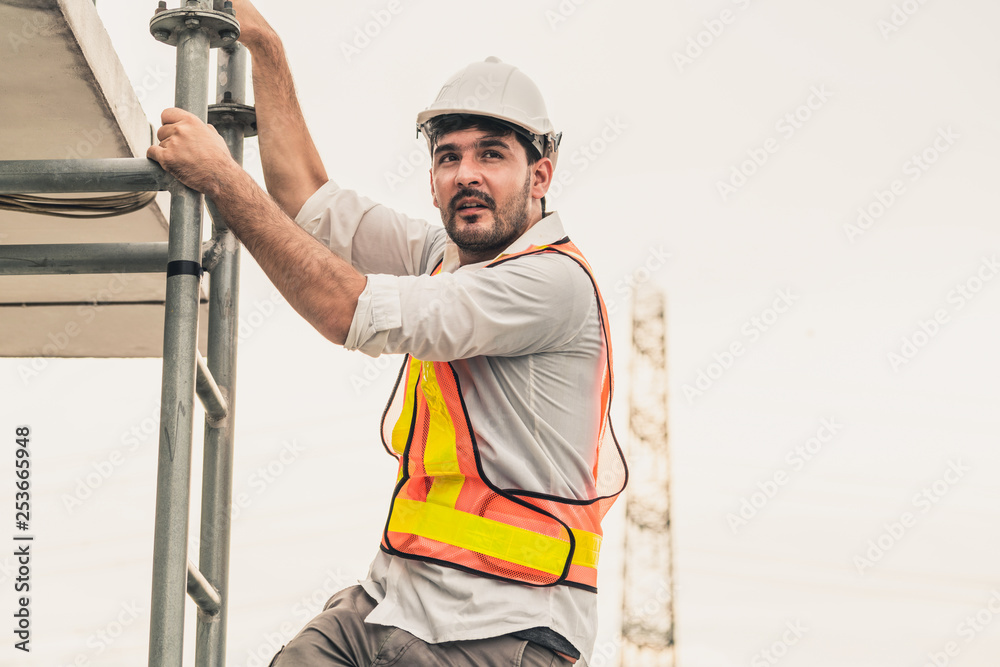 年轻的建筑工人或工程师在建筑顶部爬梯子。工程项目混凝土