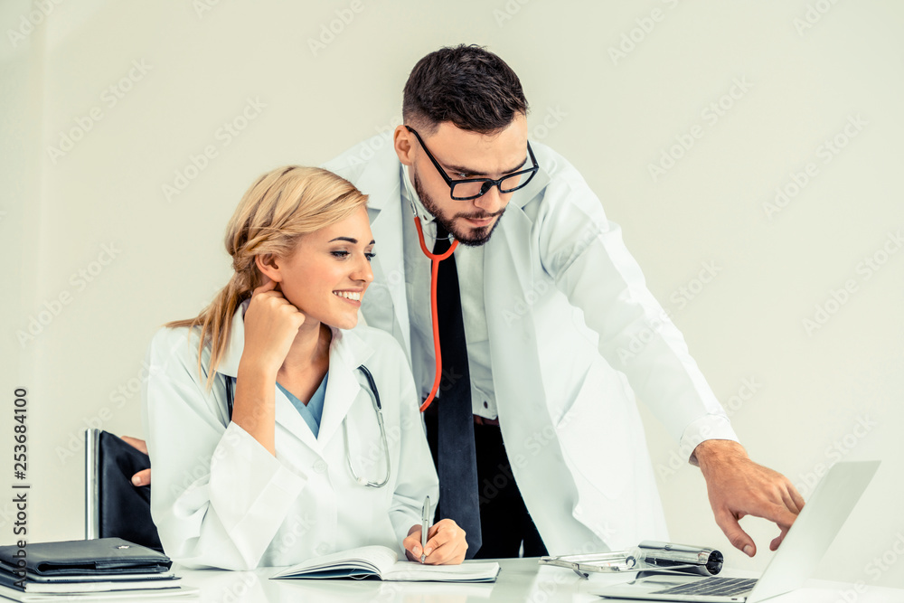 Doctor at hospital office working on laptop computer on the table with another doctor having discuss