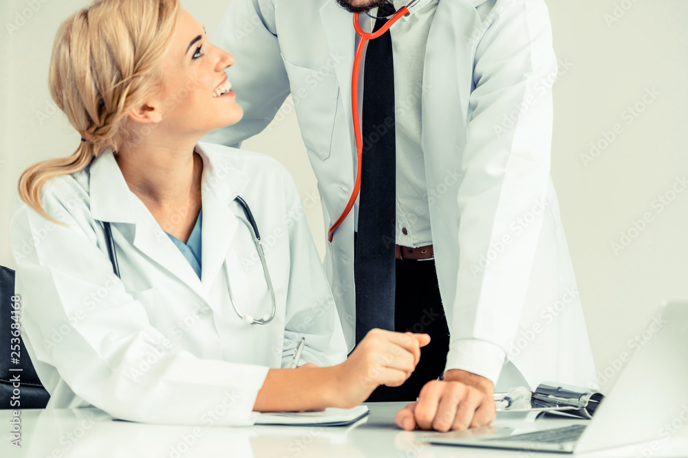 Doctor at hospital office writes notes on patients report while having conversation with another doc