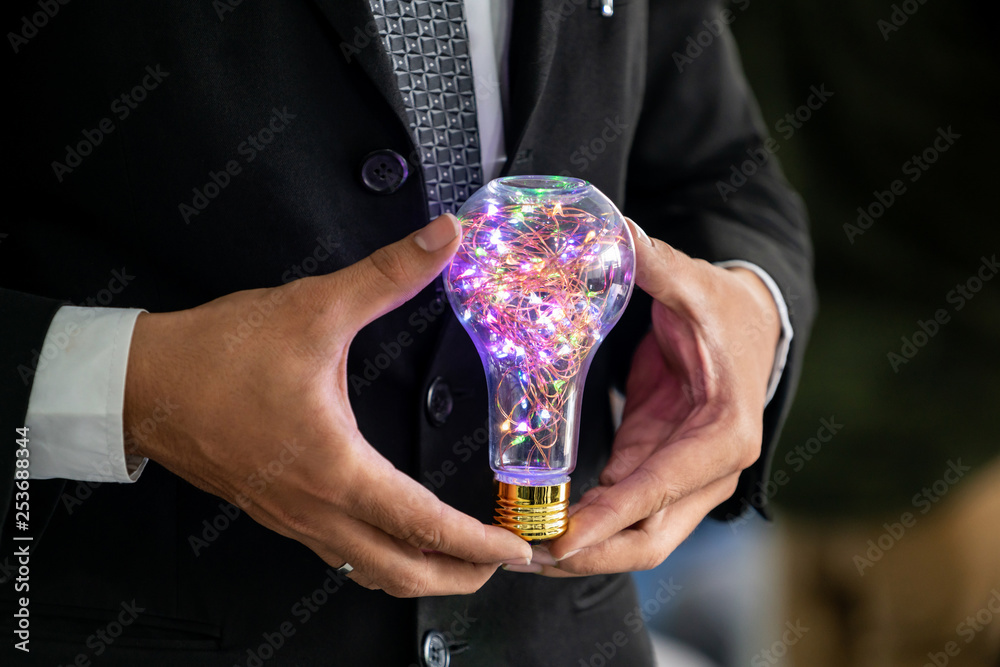 Businessman holding glowing light bulb in hands. Concept of business creativity and ideas.