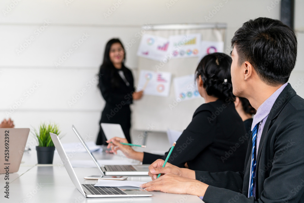 Asian business people listening to presentation from the businesswoman who stands in front of the gr