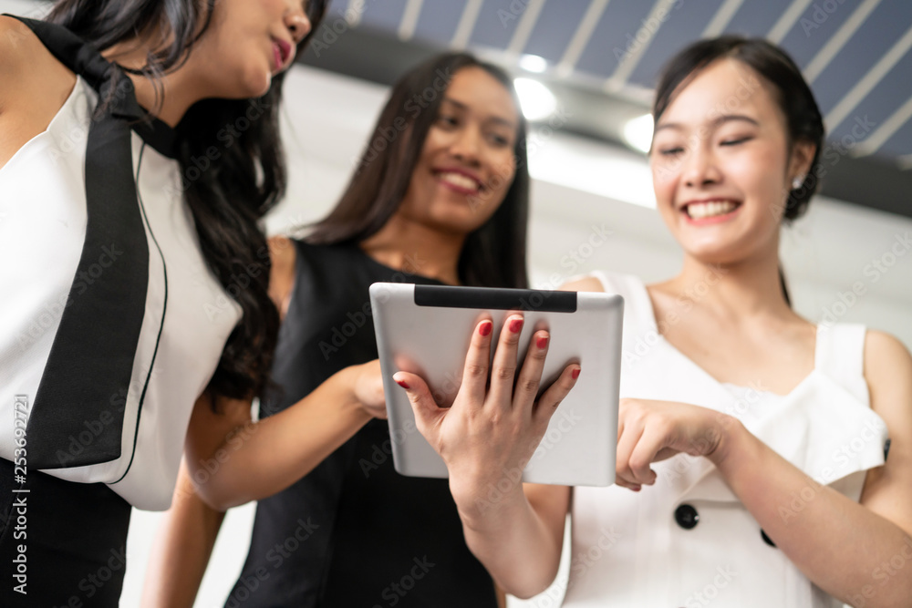 Three Asian women friends having conversation while looking at tablet computer in their hands. Conce