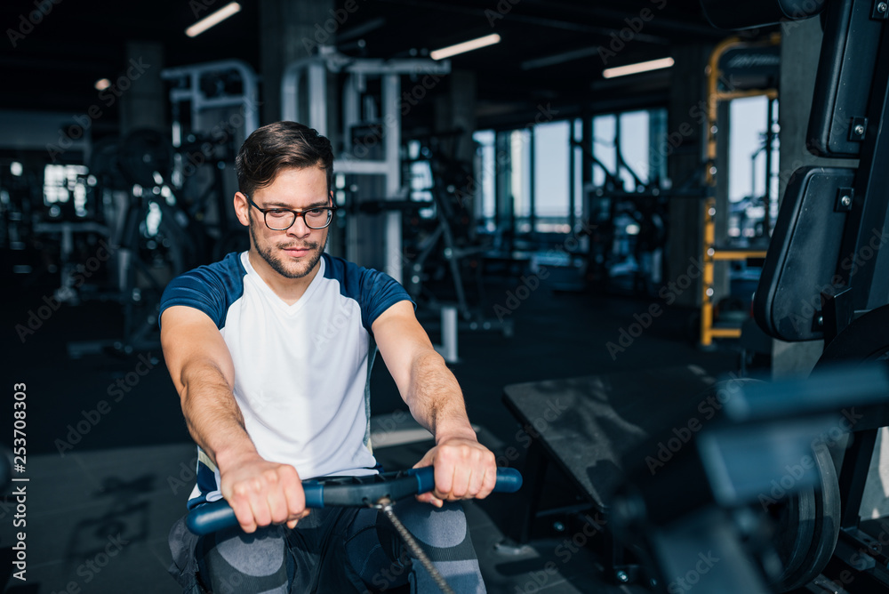 Handsome man training on row machine in the gym, front view.