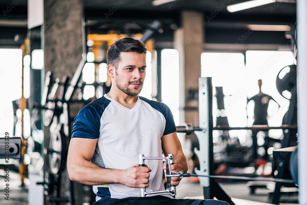 Young man working out, using a rowing pull machine to build arms muscles.