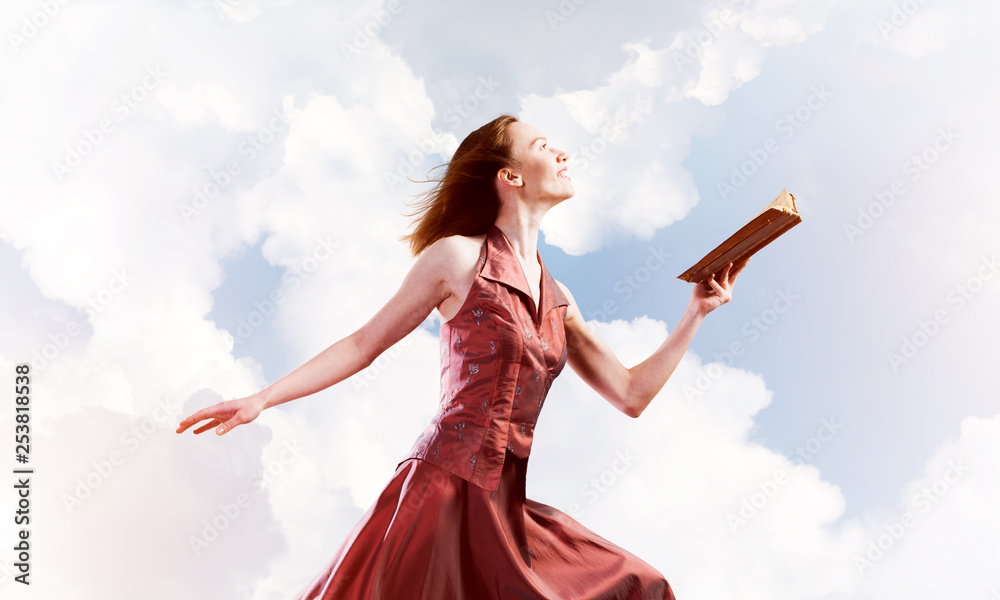 Girl against cloudy sky with opened book in palm as idea for knowledge