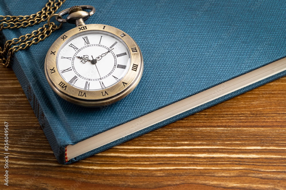 Vintage pocket watch clock with book on wooden background