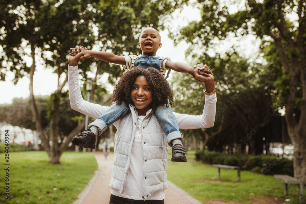 Woman giving son a piggyback ride on shoulders at park