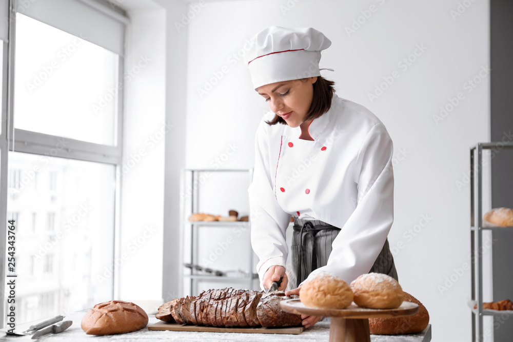 Female baker cutting fresh bread in kitchen