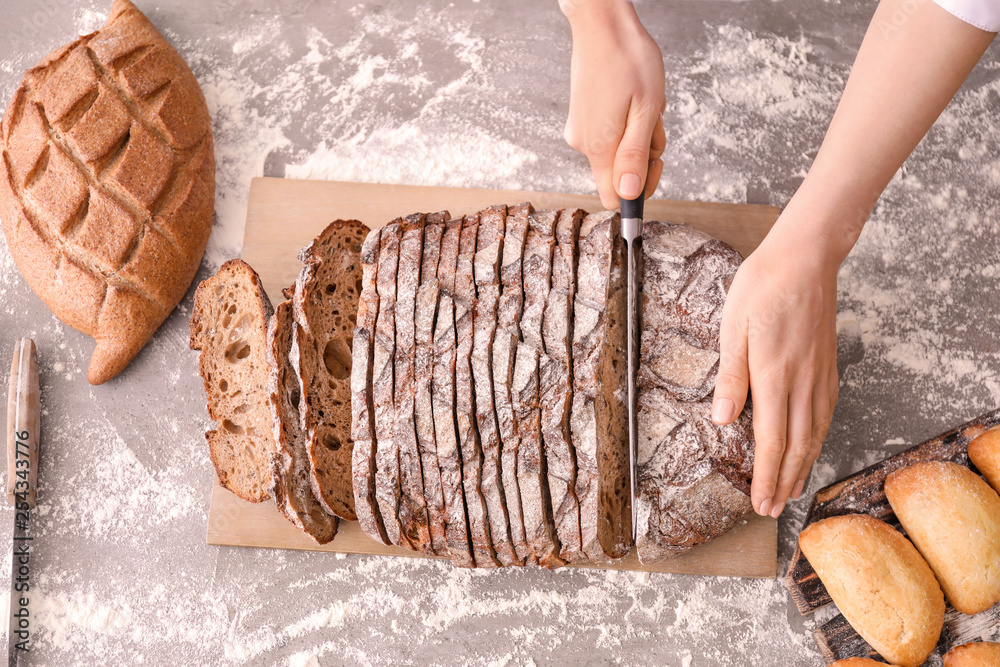 Female baker cutting fresh bread in kitchen