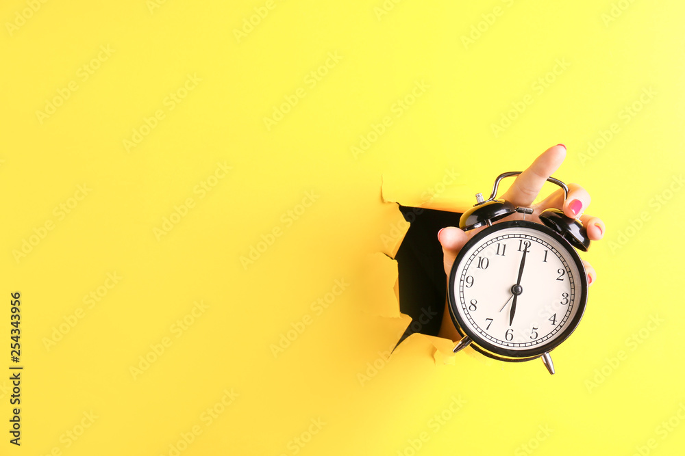 Female hand with alarm clock visible through hole in torn color paper