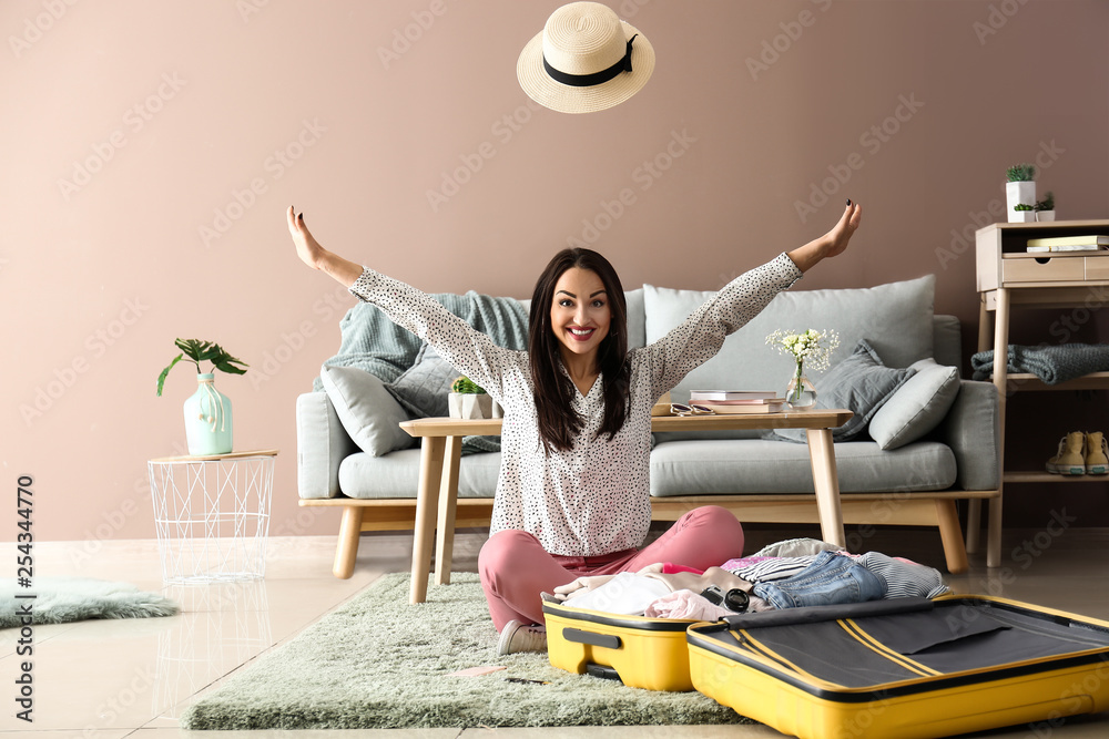 Young woman having fun while packing suitcase at home. Travel concept