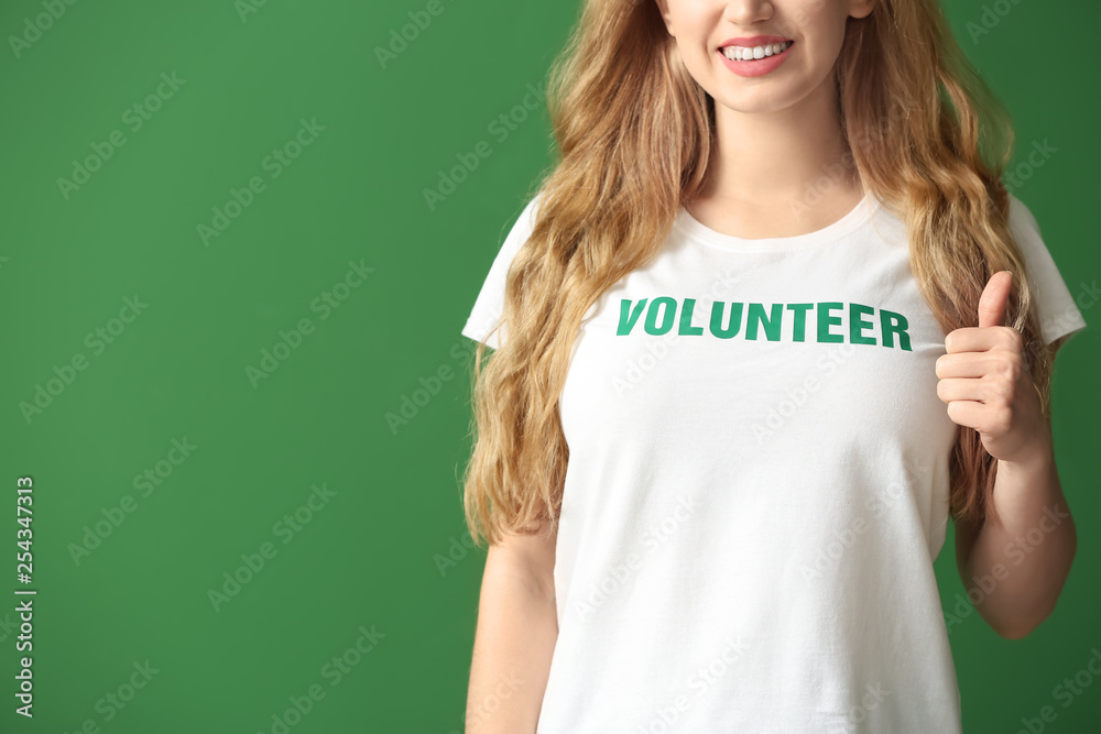 Young female volunteer showing thumb-up on color background