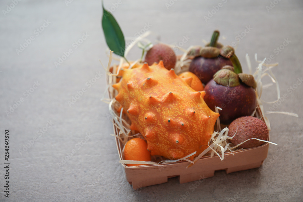 Box with assortment of tasty exotic fruits on grey background