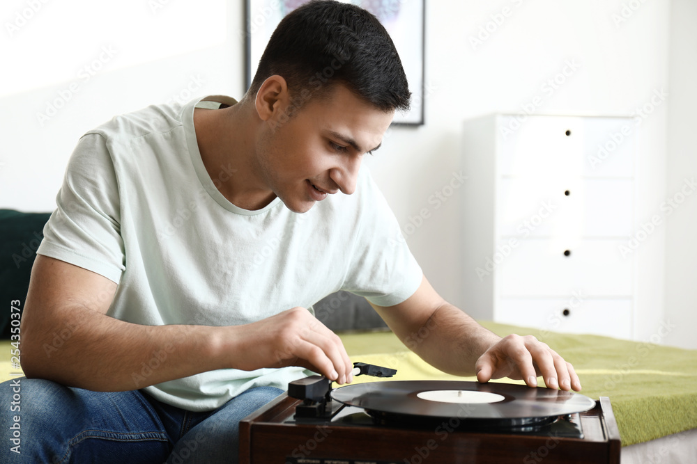 Young man listening to music on record player at home