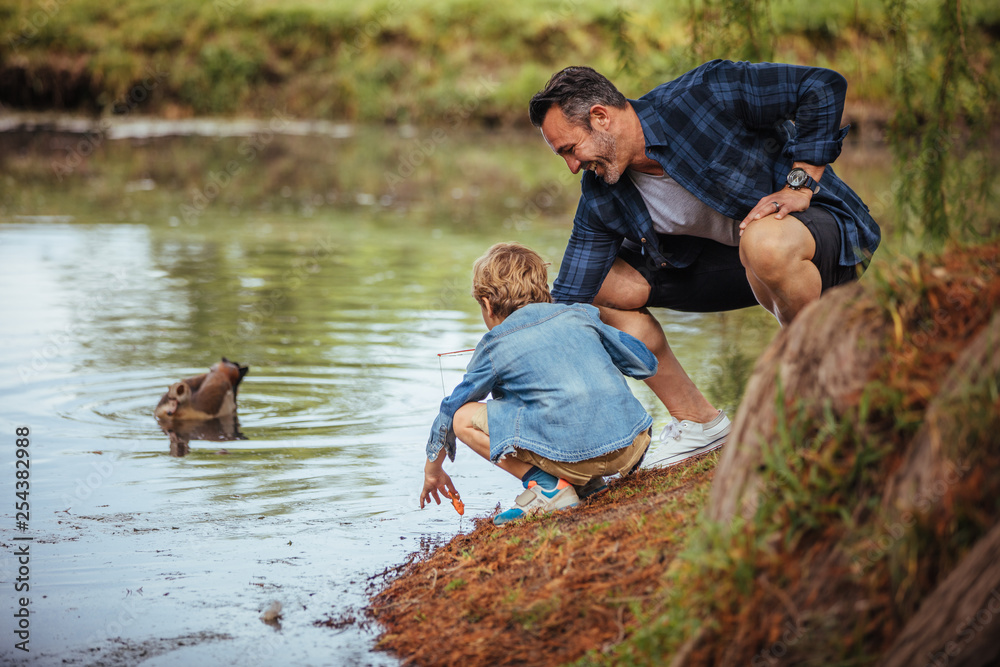 Father teaching little son fishing at pond