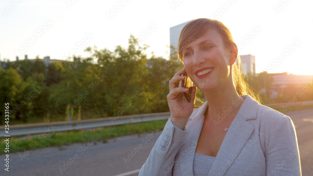 SUN FLARE: Happy businesswoman smiles while calling her friend after work.