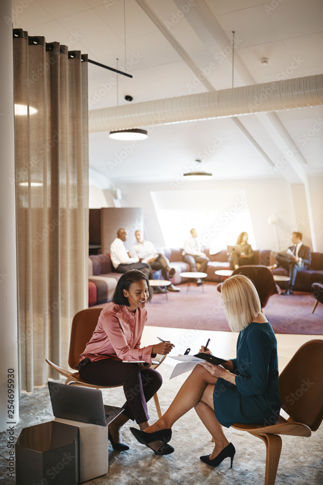 Two young businesswomen sitting in an office going over notes