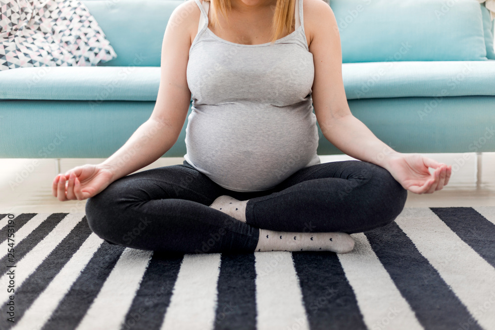 Meditating on maternity, pregnant woman meditating sitting on carpet at home