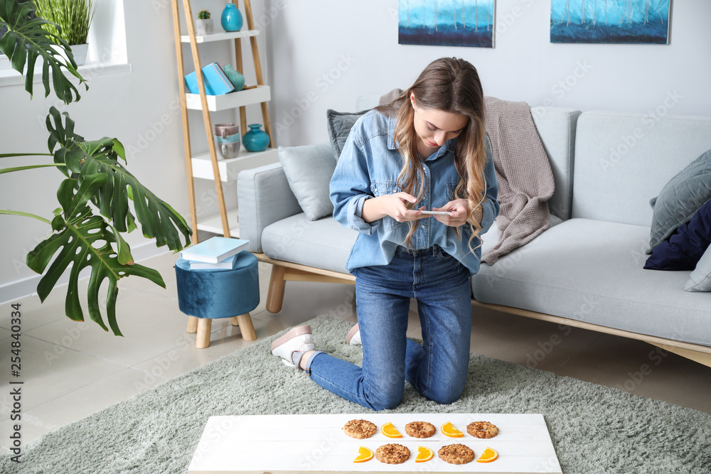 Female food photographer with mobile phone taking picture of tasty cookies and orange slices at home