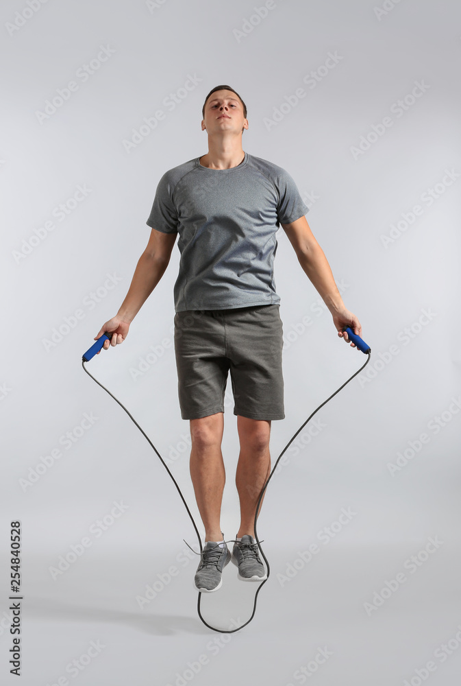 Sporty young man jumping rope against grey background