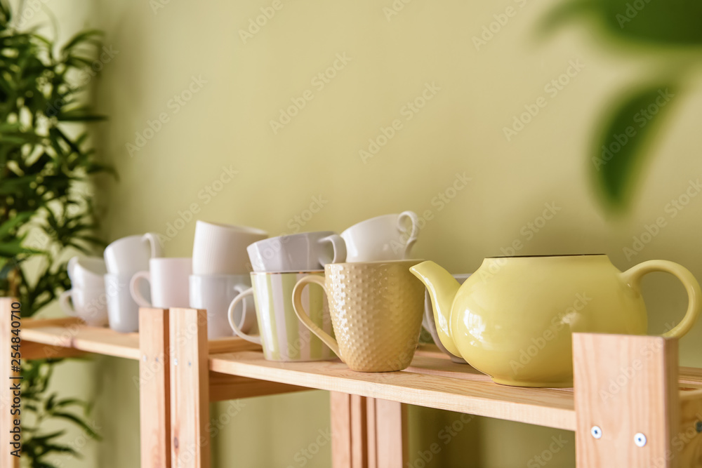 Set of clean dishes on wooden shelf near color wall