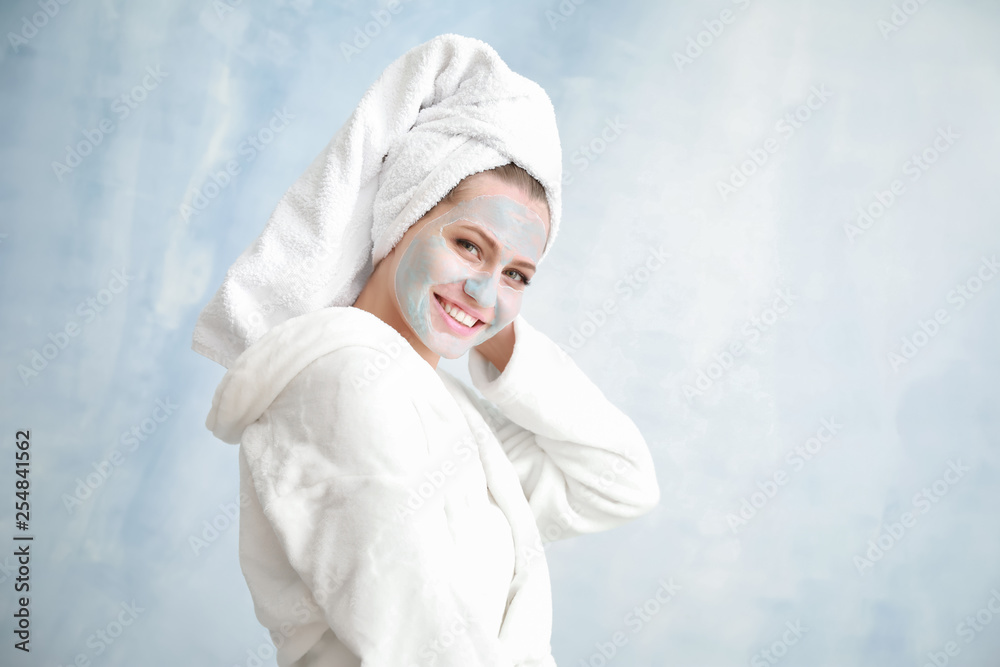 Beautiful young woman with facial mask on light background