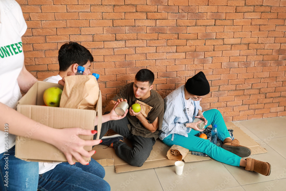 Volunteers giving food to poor people sitting near brick wall