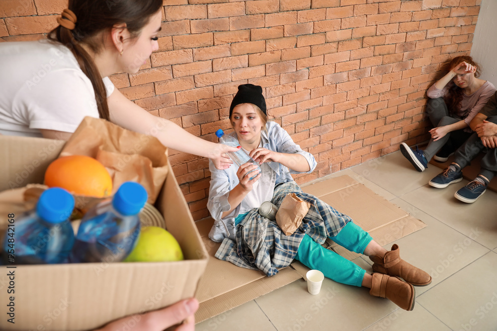 Volunteers giving food to poor people sitting near brick wall