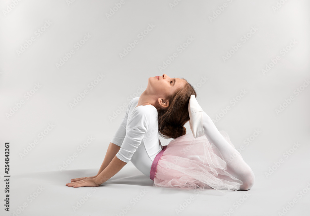 Cute little ballerina stretching against light background