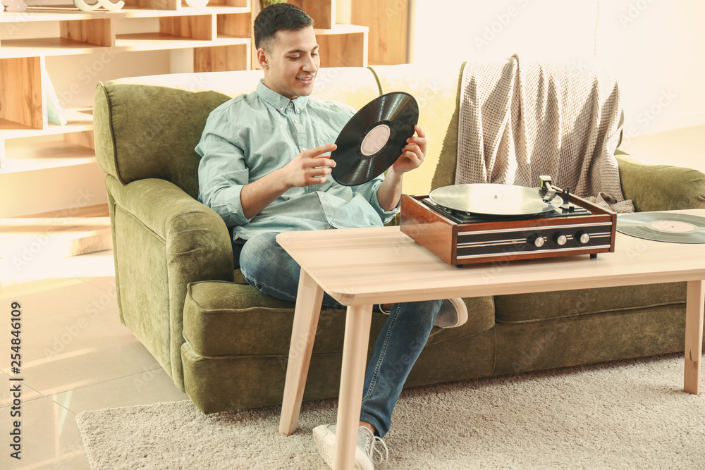 Young man listening to music on record player at home