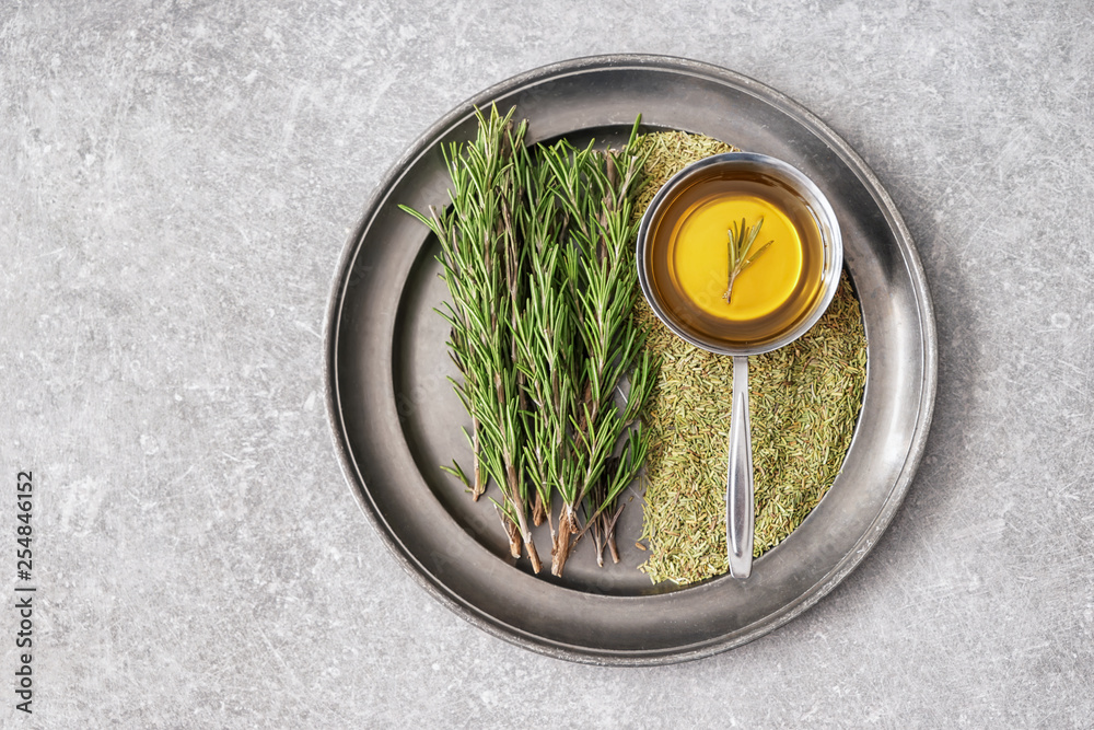 Tray with fresh and dry rosemary and oil on grey table