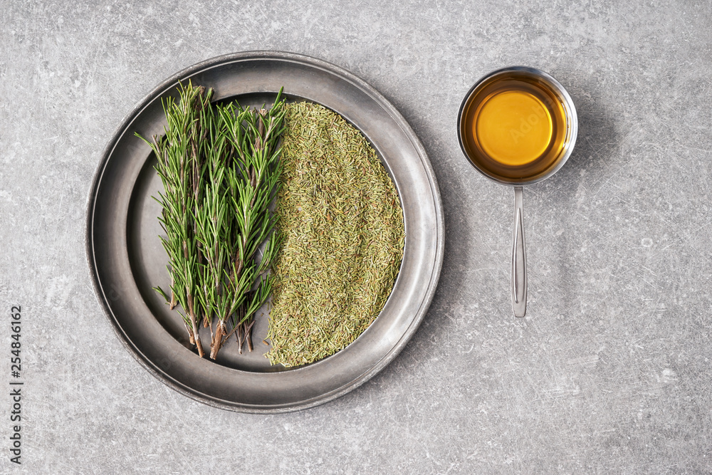 Tray with fresh and dry rosemary and oil on grey table